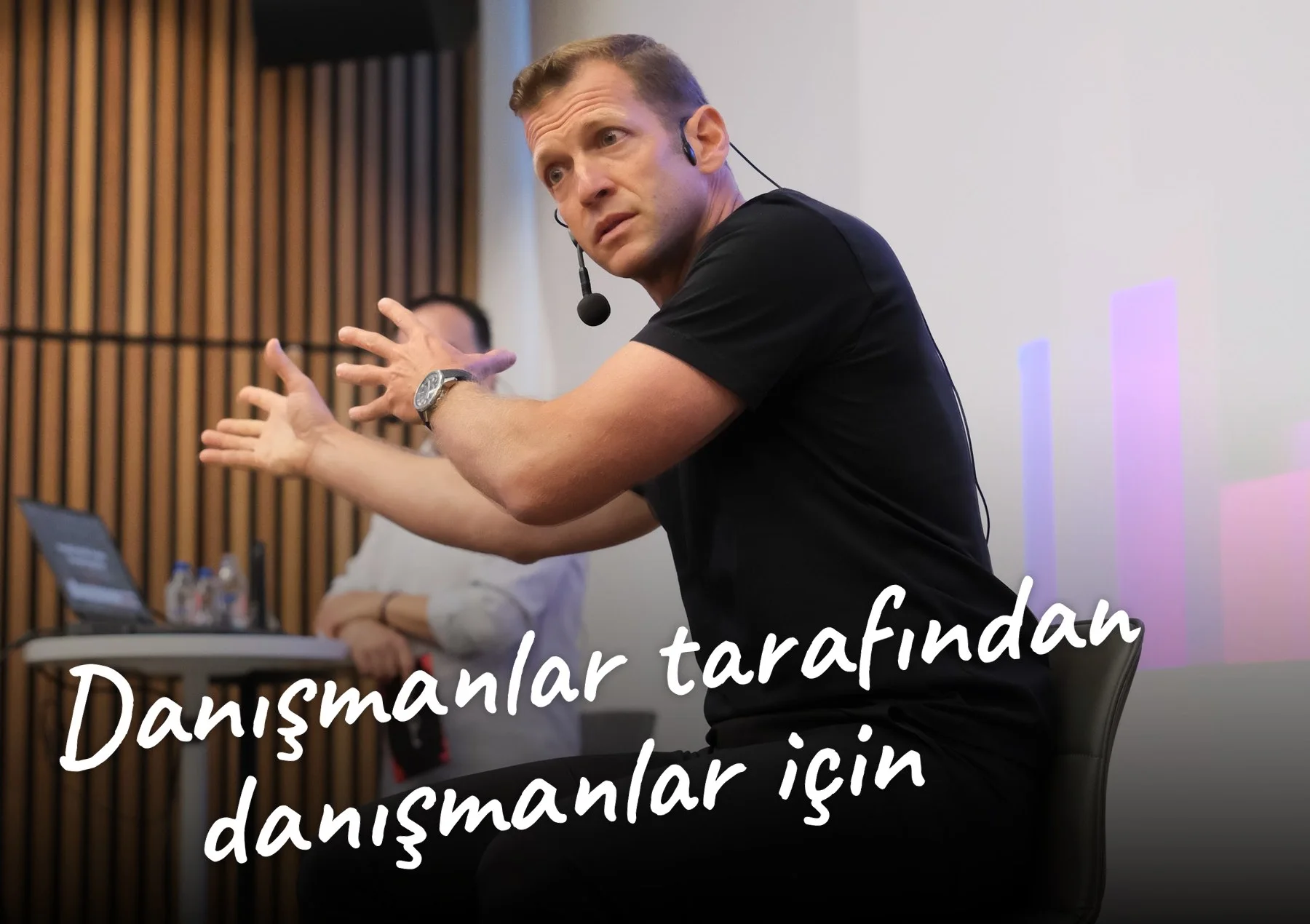 Emre Erol sahnede danışmanlara anlatırken, üzerinde Danışmanlar tarafından, danışmanlar için yazısı